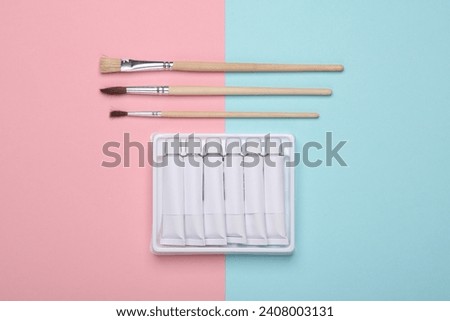 Set of white empty tubes of acrylic or oil paint and brushes for creativity on pink blue background. Template for design, mockup