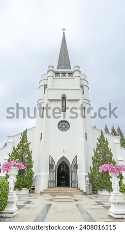 Picture of a Christian church Opening the doors to people It looks like a temple with a spire. It was painted in a striking white color. and beautifully decorated trees were planted
