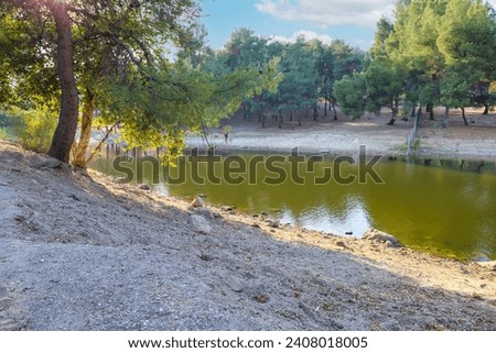 a beautiful summer landscape at Puddingstone Lake with green water surrounded by lush green trees, grass and plants in San Dimas California USA Royalty-Free Stock Photo #2408018005