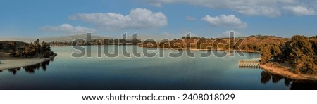 a breathtaking aerial panoramic shot of the still blue waters and lush green trees and majestic mountain ranges at Frank G Bonelli Regional Park at Puddingstone Lake in San Dimas California	 Royalty-Free Stock Photo #2408018029