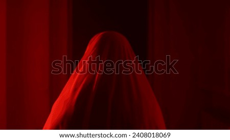 Portrait of ghost female in the house. Woman in white dress with veil covering her face walking in the corridor with red lightning