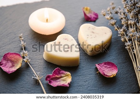 Small homemade heart shape bath melts in bathroom on black stone tray with candle burning and dried rose petals and lavender flower. Home spa concept. Royalty-Free Stock Photo #2408035319