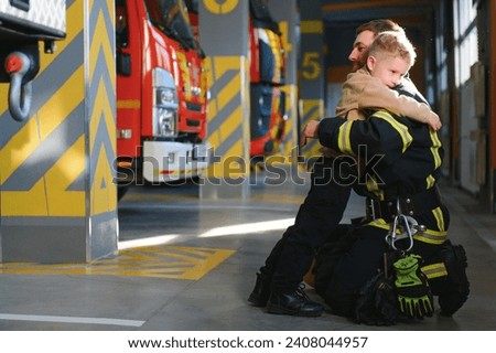 A firefighter take a little child boy to save him. Fire engine car on background.