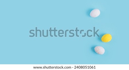 Minimalistic easter background of chocolate candy yellow and white eggs on a blue background. Top view with free copy space for text