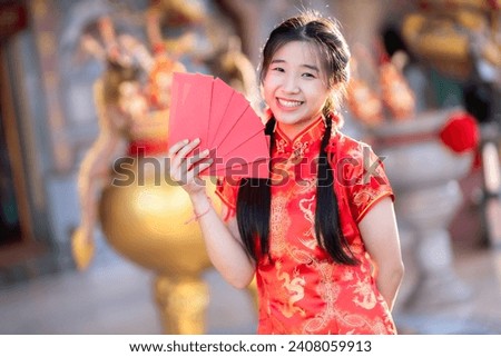 Portrait smiles Asian young woman wearing red cheongsam dress holding red envelopes decoration for Chinese new year festival celebrate culture of china at Chinese shrine Public places in Thailand