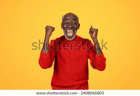 Exuberant senior african american man winner with a white beard cheering with fists pumped in the air, wearing a red sweater and a joyful expression on a sunny yellow background Royalty-Free Stock Photo #2408066803