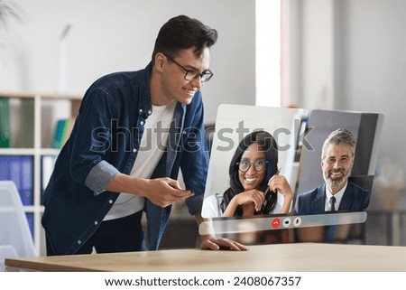 Young european businessman engaging in online conference call with diverse colleagues, displayed on large digital screen at his desk in modern office. Virtual communication. Collage Royalty-Free Stock Photo #2408067357