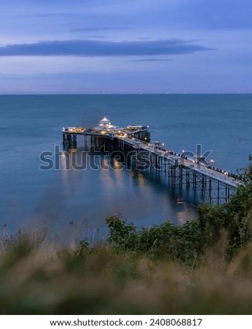 Long historic pleasure pier at dusk below dramatic cliffs. Llandudno seaside resort, North Wales Royalty-Free Stock Photo #2408068817