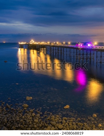 Long historic pleasure pier at dusk with lights reflecting in the water. Llandudno seaside resort, North Wales Royalty-Free Stock Photo #2408068819