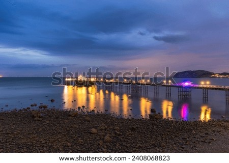 Long historic pleasure pier at dusk with lights reflecting in the water. Llandudno seaside resort, North Wales Royalty-Free Stock Photo #2408068823