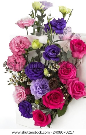 beautiful bouquet of flowers in a box, close-up with a blurred white background, as a gift. red roses, pink and purple eustoma, cones, greens, butterfly