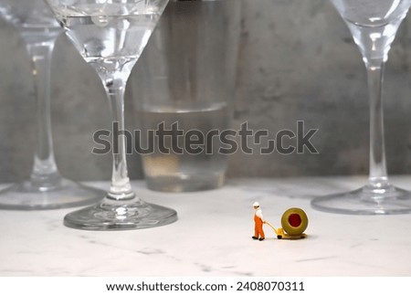 Miniature Worker Dragging Cocktail Olive Across Stone Bar with Hand Dolly. Royalty-Free Stock Photo #2408070311