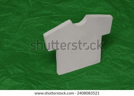 Concrete material t-shirt icon isolated on green crumpled paper background. Unique creative photo for website, internet marketing, presentation, logo design template element.