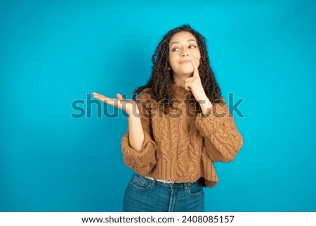 Positive Beautiful girl with curly hair wearing brown knitted sweater advert promo touch finger teeth