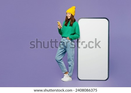 Full body side view young woman she wears green sweater yellow hat casual clothes big huge blank screen mobile cell phone with area using smartphone isolated on plain pastel light purple background