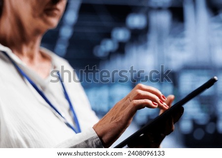 Senescent IT manager using tablet, ensuring valuable data remains shielded from potential perils, safeguarding supercomputers against unauthorized access and vulnerabilities, close up Royalty-Free Stock Photo #2408096133