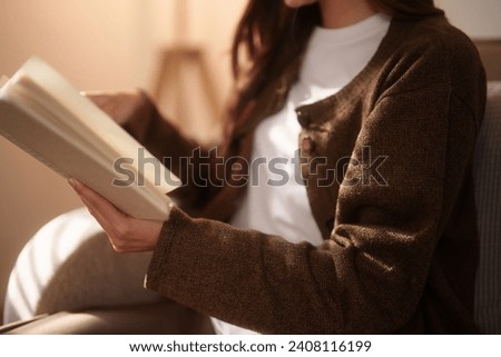 Young asian women sitting on comfortable the couch to opening the book and reading literature while enjoying and happiness for relaxation time in living room with lifestyle at home. Royalty-Free Stock Photo #2408116199