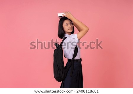 Asian female student presenter for world education Lift the textbook on your head. carrying a school bag Study at famous schools and tutoring institutes Taking photos in a pink background studio