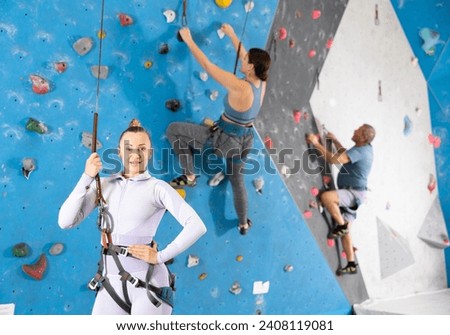 Adult woman in sportswear posing with safety rope at climbing wall