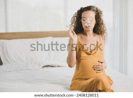 Curly hairstyle young unhappy unhealthy bad behavior Caucasian pregnancy mother in maternity long dress cloth sit on bed in bedroom holding smoking cigarette taking risk and danger to unborn child. Royalty-Free Stock Photo #2408128011