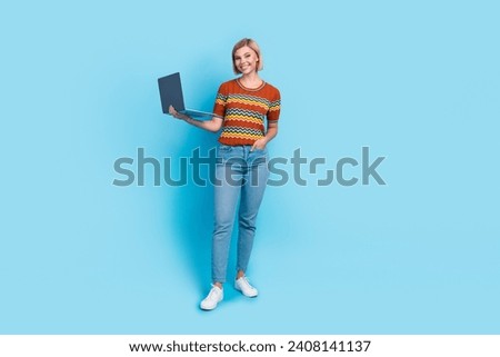 Full size photo of intelligent gorgeous girl wear striped t-shirt jeans holding laptop arm in pocket isolated on blue color background
