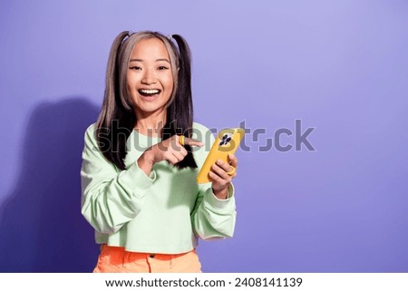 Photo of kpop fan youngster girl wearing green sweatshirt point finger demonstrating mobile phone isolated on purple color background