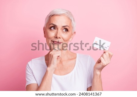 Photo portrait of lovely senior lady credit card look minded empty space dressed stylish white garment isolated on pink color background