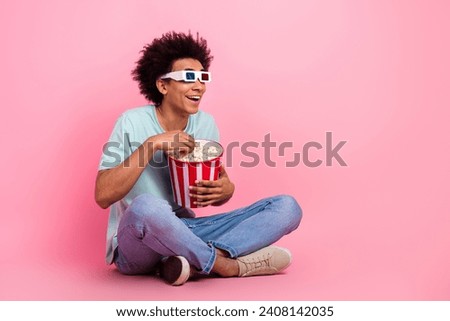 Full body photo of attractive young man sit floor eat popcorn watch film dressed stylish blue clothes isolated on pink color background