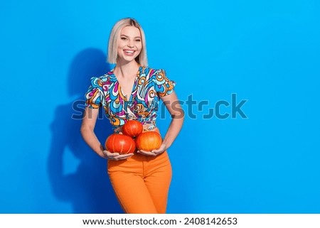 Photo of toothy beaming girl with bob hair dressed print shirt holding squashes preparing for halloween isolated on blue color background