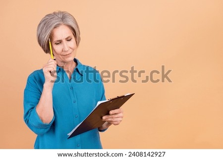 Photo of minded puzzled woman with bob hairdo dressed blue shirt look at clipboard pencil on forehead isolated on pastel color background