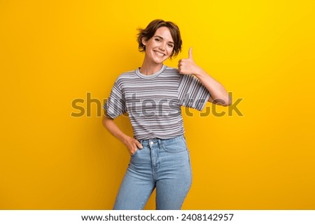 Photo of satisfied nice woman dressed striped t-shirt showing thumb up good work arm in pocket isolated on yellow color background