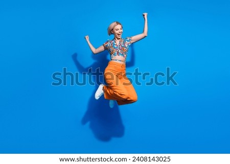 Full length photo of overjoyed lovely girl dressed print top flying raising fists up win lottery isolated on blue color background