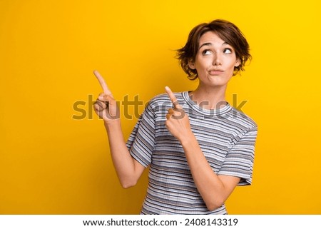 Portrait of thoughtful girl with short hair wear grey t-shirt directing look at promo empty space isolated on yellow color background