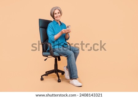 Full size photo of smart pleasant woman dressed stylish shirt sit on armchair with smartphone in hands isolated on pastel color background