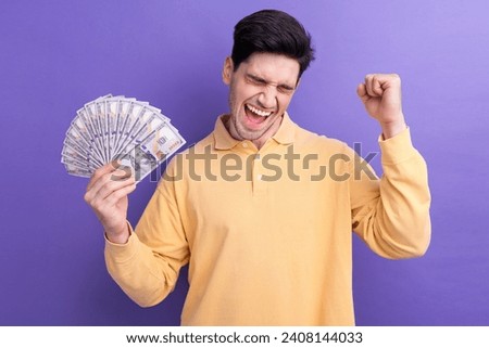 Photo of dreamy lucky man dressed yellow shirt rising dollars fan winning prize isolated purple color background