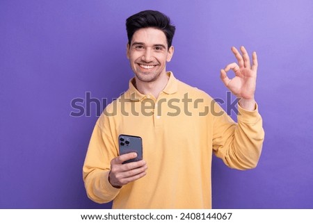 Photo of cheerful attractive guy wear yellow polo reading news modern gadget showing okey isolated violet color background