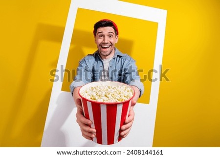 Photo of good mood cheerful man dressed jeans shirt inviting you eating pop corn tacking photo frame isolated yellow color background