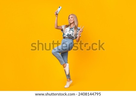 Full length photo of cheerful woman wear blouse denim pants making selfie on smartphone show v-sign isolated on yellow color background