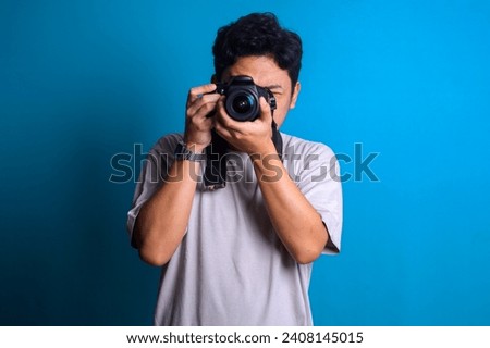 Young professional photographer in red shirt take picture of you using camera on blue background
