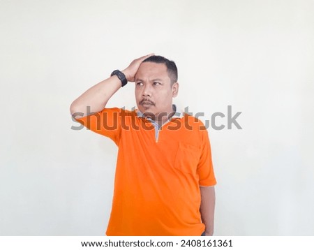 Asian adult male in orange t-shirt making gestures and facial expressions on white background Royalty-Free Stock Photo #2408161361