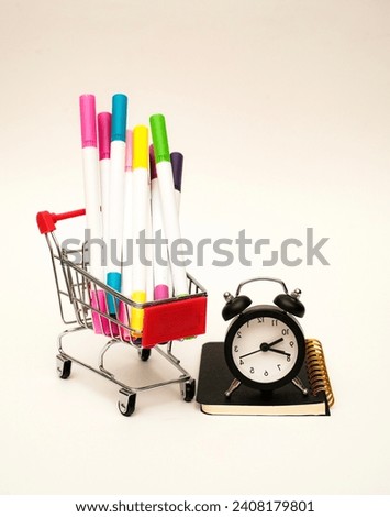 A bunch of colourful pens in the trolley sitting next to a black alarm clock on the notebook. Back to school concept