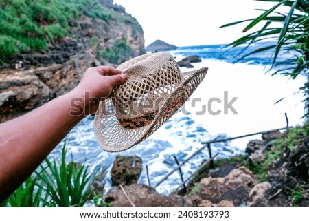 Hand of Man Holding Straw Cowboy Hat on Rock Coral and Ocean at Jogan Beach Gunung Kidul Yogyakarta Indonesia