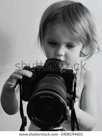 A curious young girl with focused attention is pictured in a monochrome setting, exploring the functionalities of a large professional camera