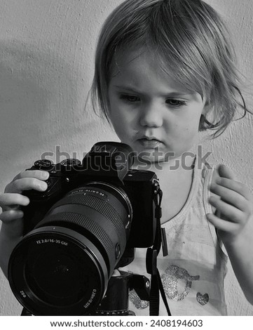 A curious young girl with focused attention is pictured in a monochrome setting, exploring the functionalities of a large professional camera
