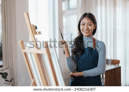 Happy asian woman artist drawing picture on canvas in studio.