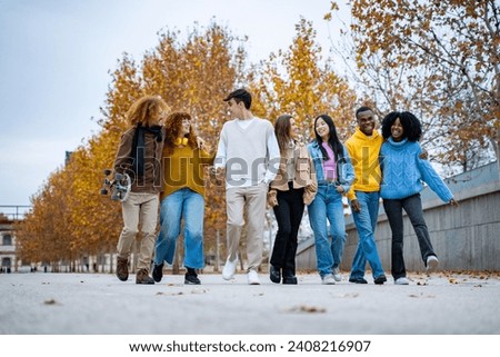 Happy, diverse friends walking together, surrounded by the golden hues of fall leaves, exuding warmth and unity. Royalty-Free Stock Photo #2408216907