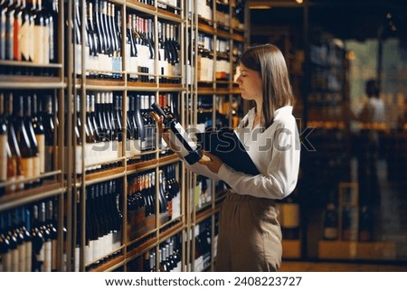 Professional female sommelier working in winery and making notes on tablet being in wine cellar. Winemaking school and tasting alcoholic beverages. Royalty-Free Stock Photo #2408223727