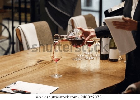 Professional female sommelier pours red wine from decanter to the glass, close up image. Woman waiter pouring alcoholic drink being in cellar of wine shop. Royalty-Free Stock Photo #2408223751