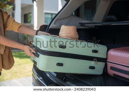  woman packing her suitcase into the car trunk.