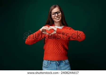 Friendly 30 year old woman with brown hair wearing a red sweater showing a heart gesture